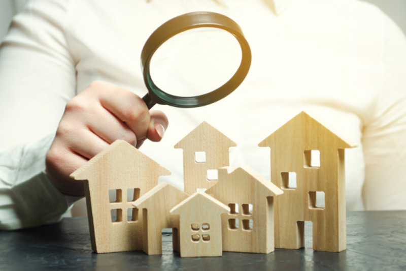 Immobilienmakler Oberursel hält eine Lupe über mehrere Holzhäuser um eine Immobilienbewertung anzudeuten